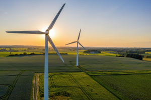 Das Bild zeigt zwei Windräder. Die Sonne geht hinter einem der Windräder unter.